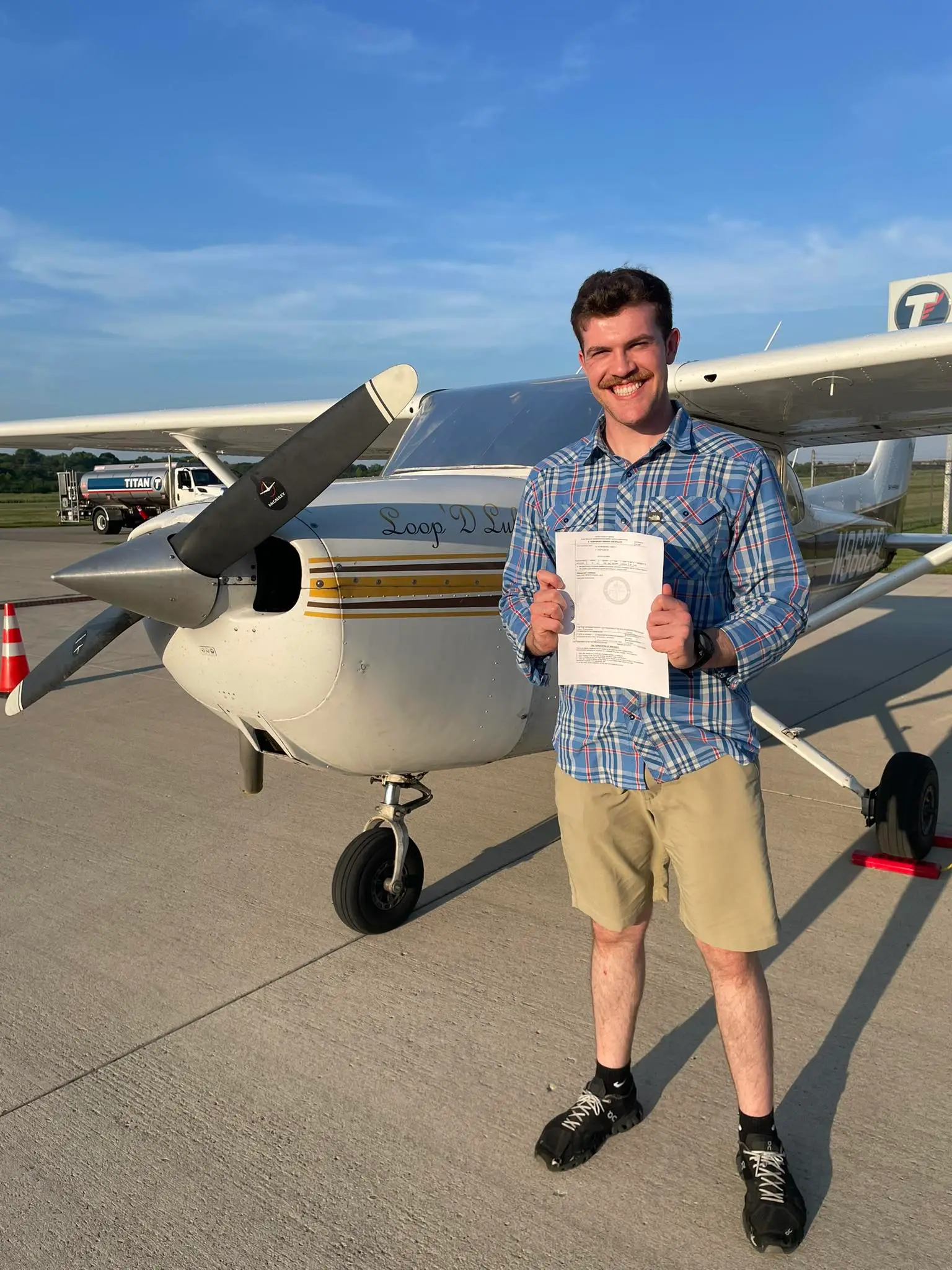 Newly certificated pilot holding a certificate in front of a Cessna training aircraft