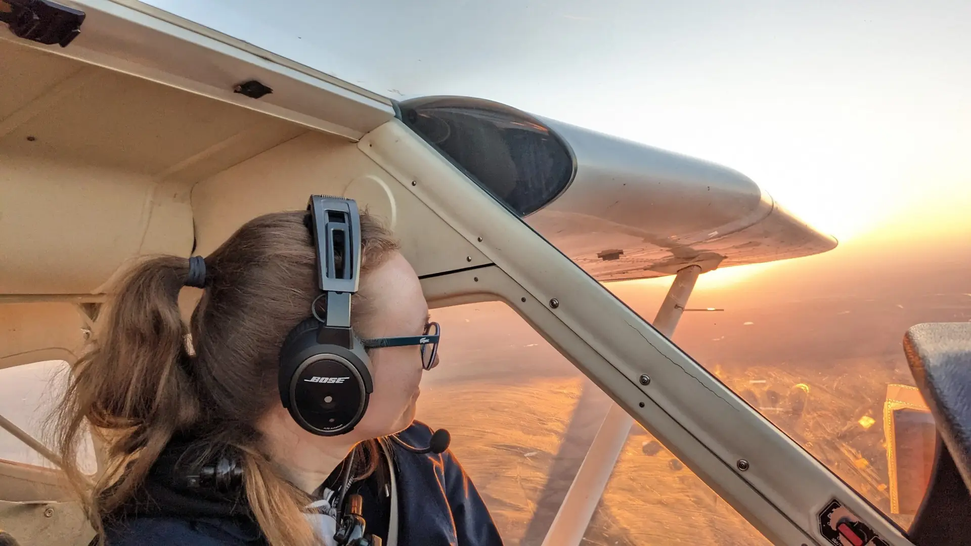 Woman pilot looking through airplane window during flight at sunset